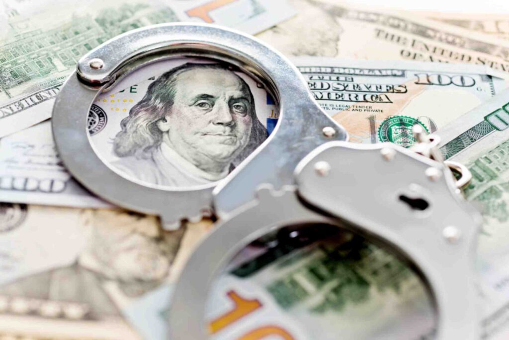 A set of handcuffs on top of several bills of money. 